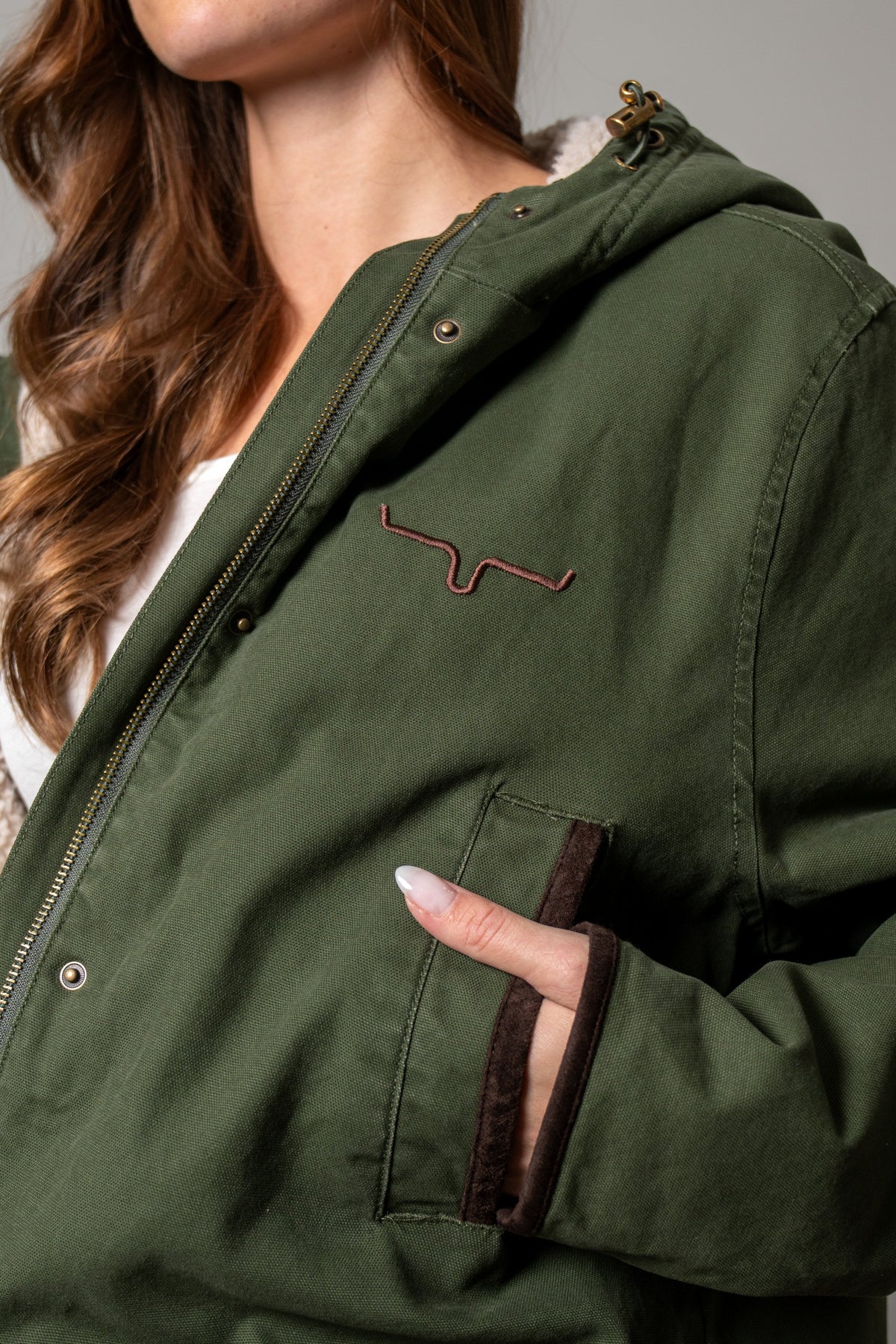 Kimes Ranch Emery jacket in moss with brass hardware, hood, Kimes Ranch logo, and pocket with brown suede trim
