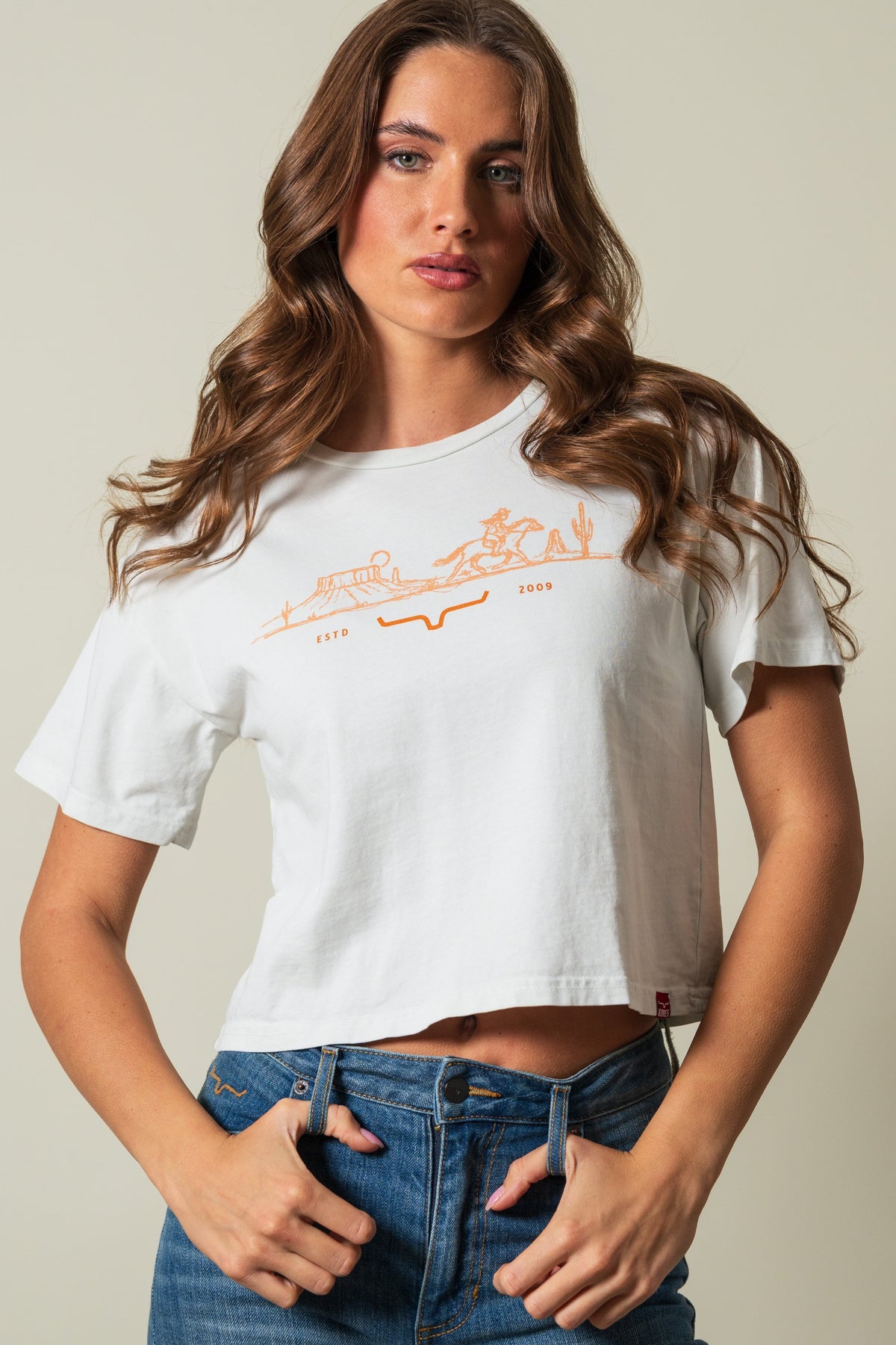 Kimes Ranch Go West Natural shirt with orange graphic of a rider and landscape reading ESTD 2009