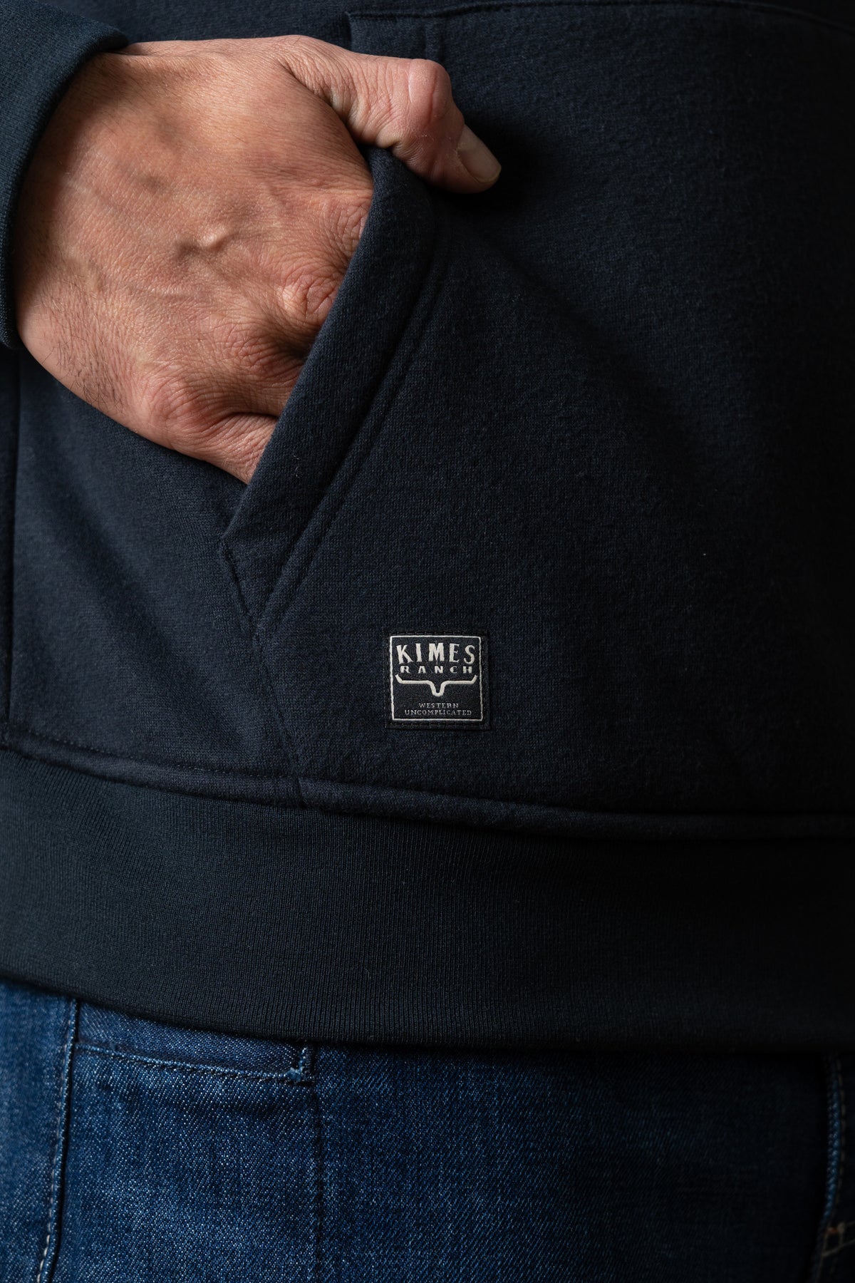 Kimes Ranch Mallard black hoodie, hand in kangaroo pocket, Kimes Ranch logo patch