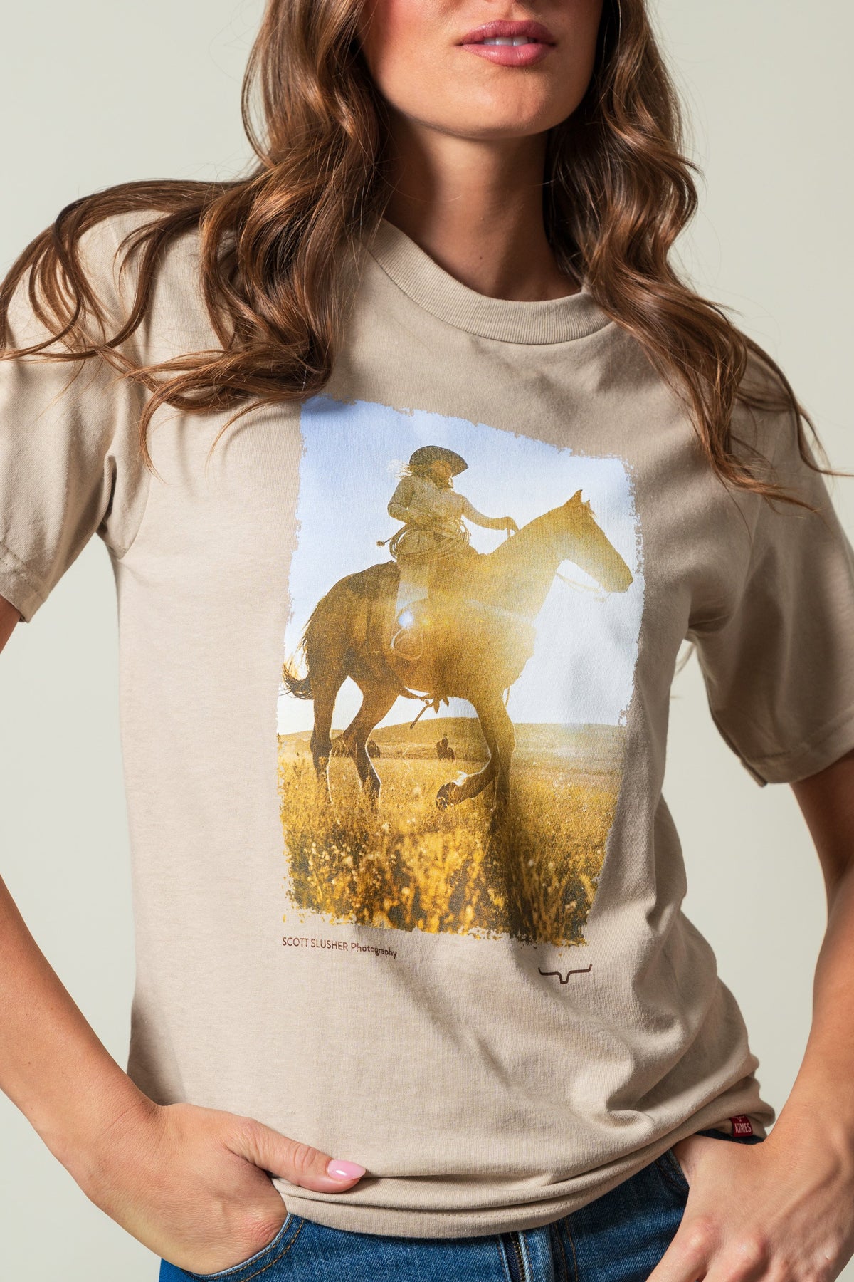 Kimes Ranch SS Riding Sunshine t-shirt in Sand with a graphic of a rider on a horse and SCOTT SLUSHER Photography text