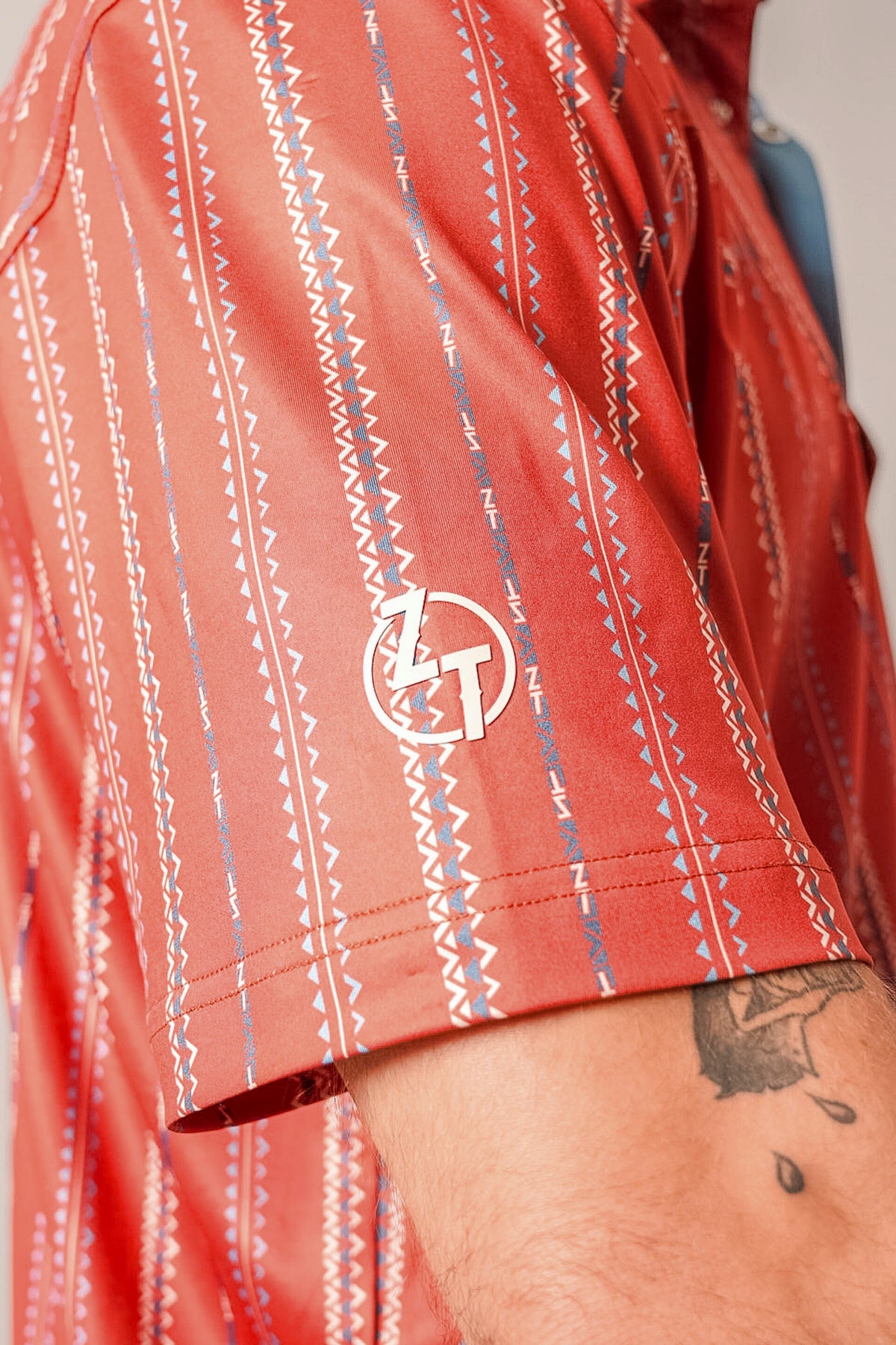 Kimes Ranch ZT Z-Stripe polo in Brick Red with a close-up of the sleeve showing the ZT logo and geometric pattern