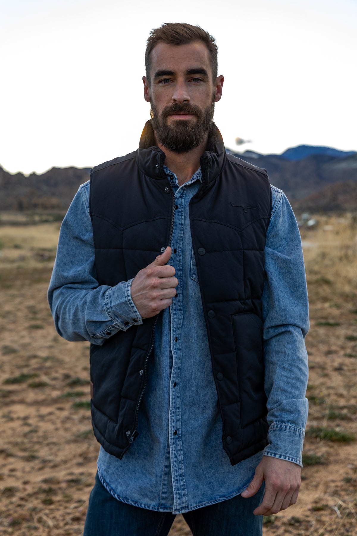 Kimes Ranch Muir Trail Vest in Black with a stand collar, front zip, snap pockets, and the Kimes Ranch logo on the chest