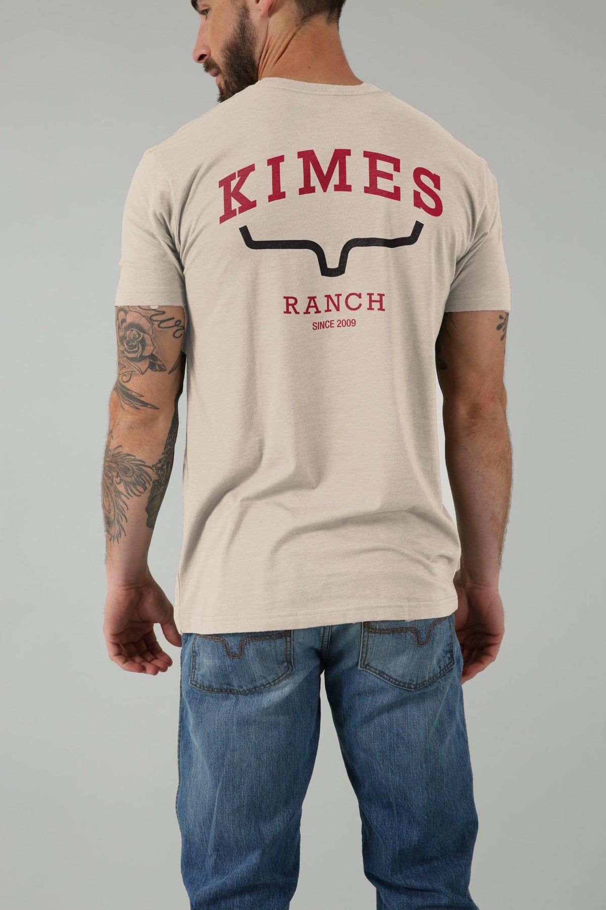 Kimes Ranch Since 2009 Shirt in Sand, back view, with back graphic featuring Kimes Ranch logo and text