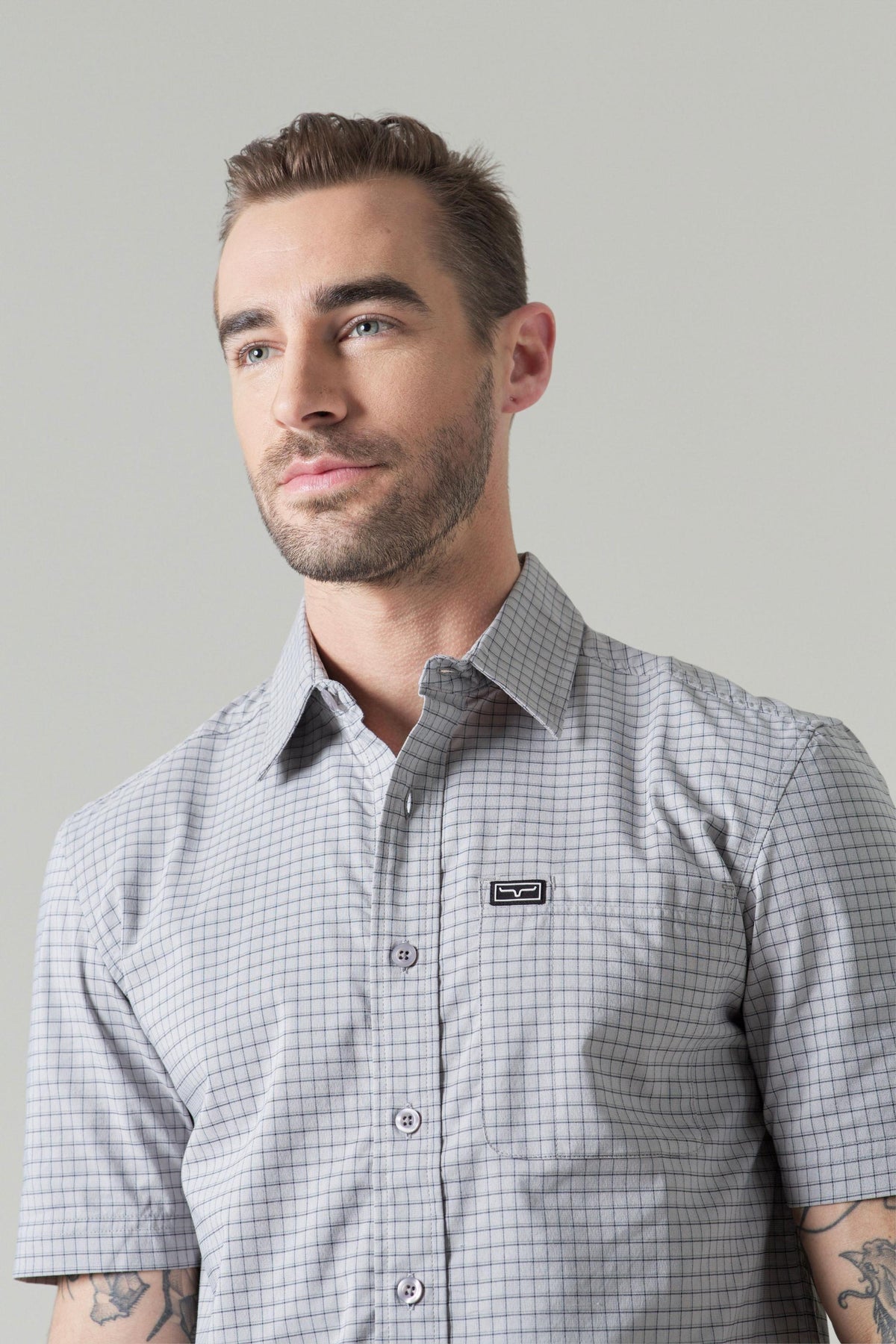 Kimes Ranch Spyglass Short Sleeve Dress Shirt in Grey with a check pattern and a chest pocket with the Kimes Ranch logo